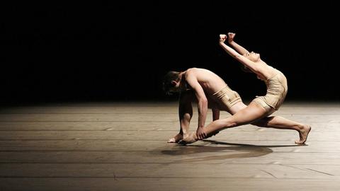 Eine Frau und ein Mann tanzen modernen Tanz auf einer dunklen Bühne.