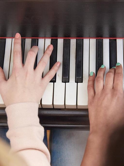 Die Hände von zwei jungen Mädchen auf den schwarz-weißen Klaviertasten.