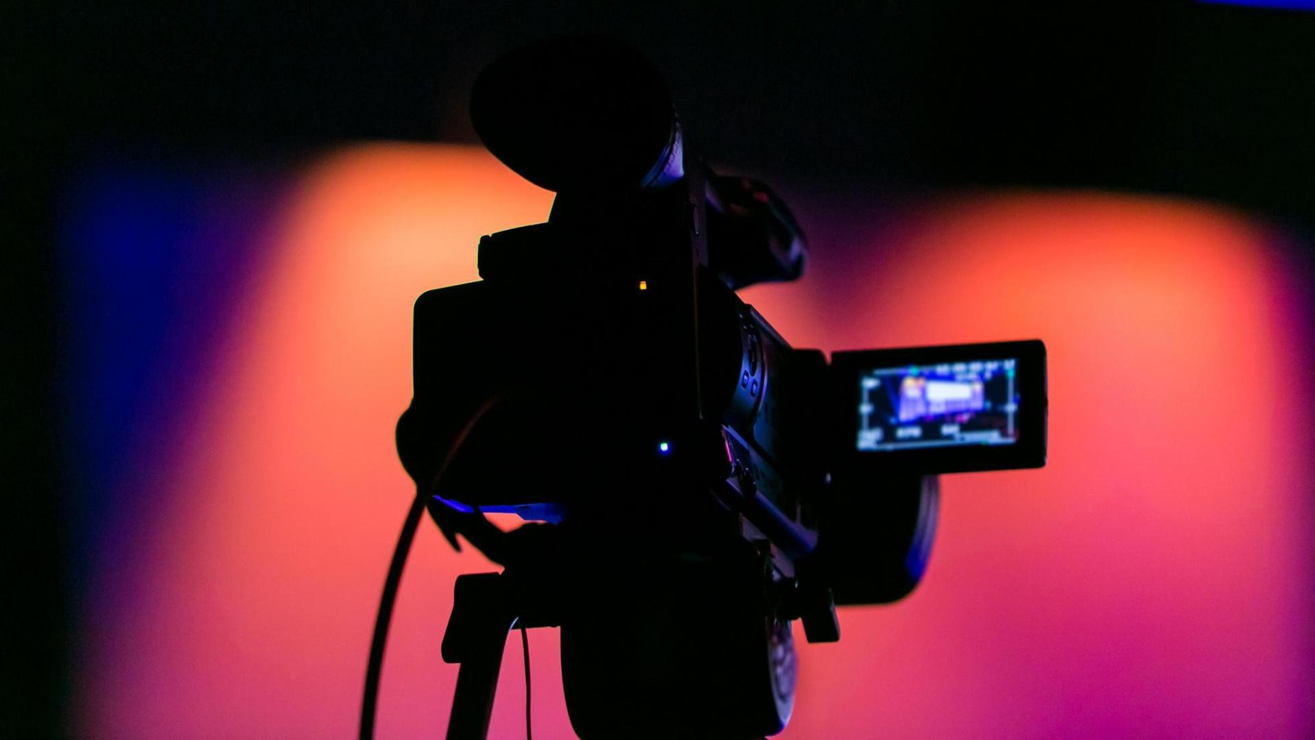 Silhouette einer Filmkamera vor buten Bühnenlichtern.