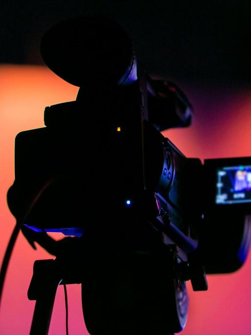 Silhouette einer Filmkamera vor buten Bühnenlichtern.