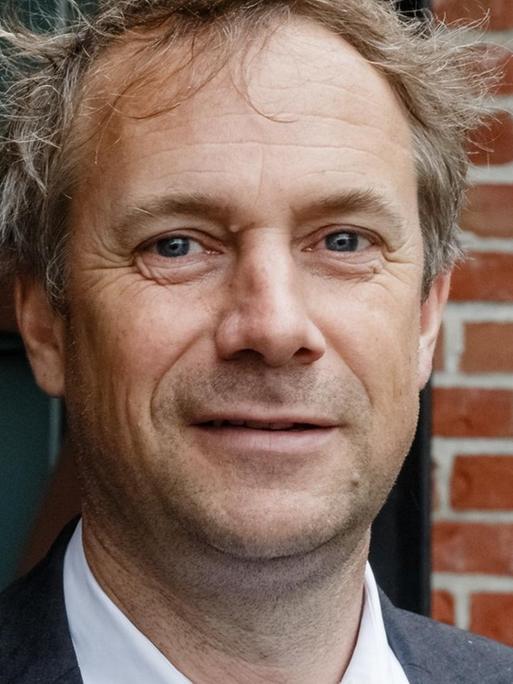 Jo Lendle, Verleger des Hanser Verlags, steht vor einer Wand aus Backstein und blickt in die Kamera.