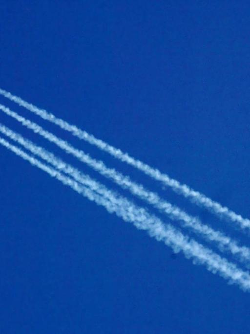 Ein Flugzeug hinterlässt Kondensstreifen vor einem blauen und wolkenlosen Himmel.