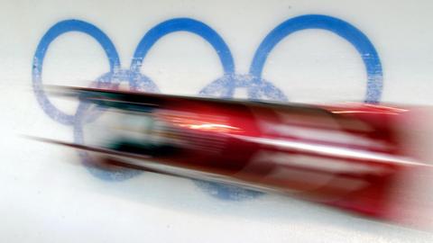 Der Zweierbob von Monaco mit Patrice Servelle an den Lenkseilen ist am 14.02.2002 bei den XIX. Winterspielen von Salt Lake City im Rahmen des Abschlusstrainings für die olympische Zweierbob-Entscheidung beim dritten Lauf durch den Eiskanal unterwegs und saust über das ins Eis der Bahn eingelassene Logo der Olympischen Ringe hinweg.