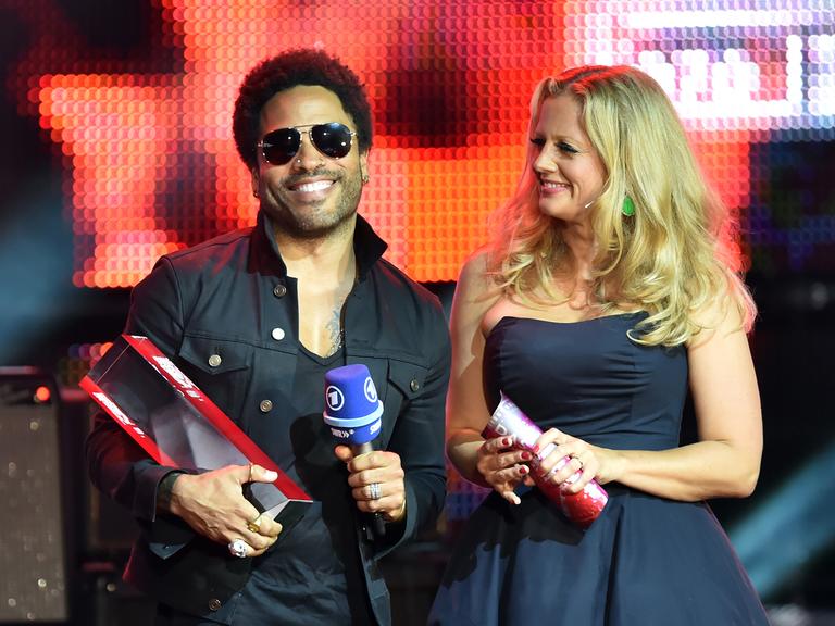 Lenny Kravitz hält den Preis auf der Bühne in den Händen, rechts daneben steht die Moderatorin Barbara Schöneberger.
