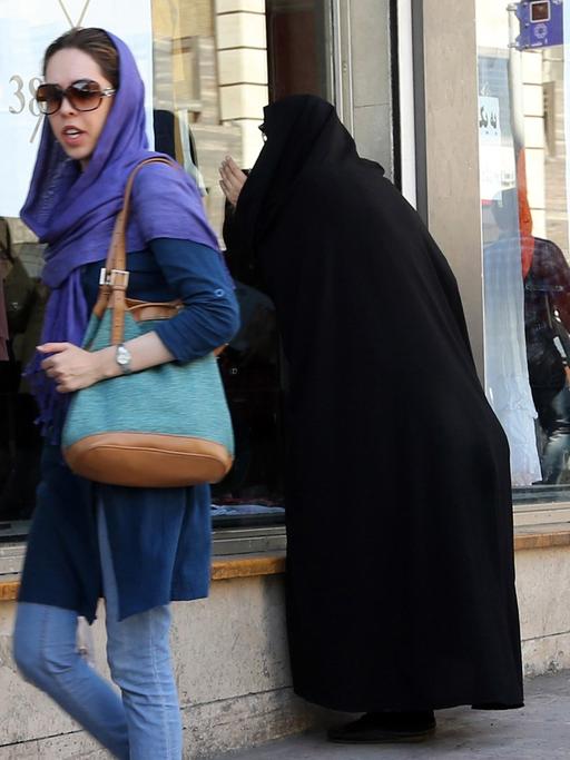 Junge Iranerinnen in Jeans und bunten Tüchern gehen mit Einkaufstüten eine Straße entlang.
