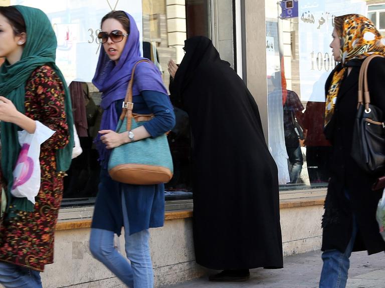 Junge Iranerinnen in Jeans und bunten Tüchern gehen mit Einkaufstüten eine Straße entlang.