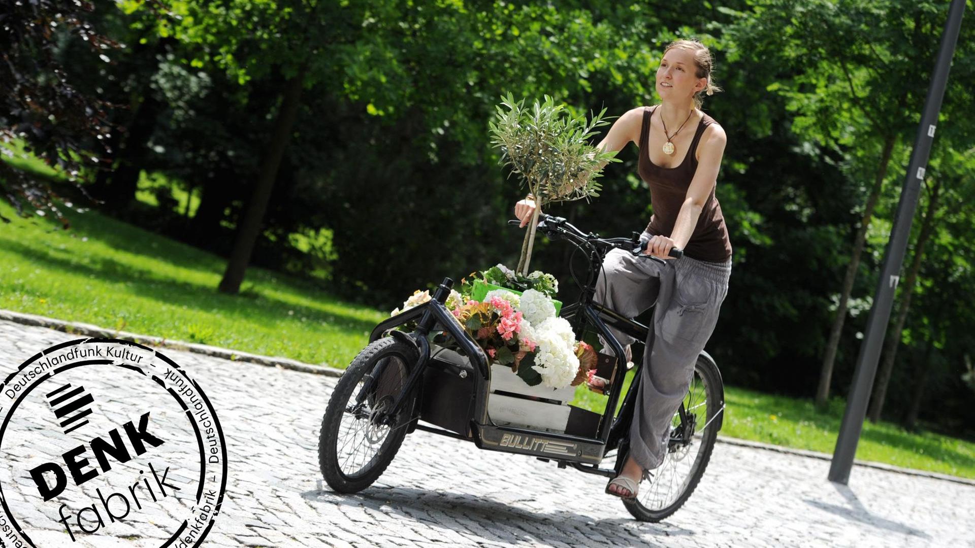 Eine Frau fährt mit einem Transportrad, das mit Blumen beladen ist. Mit Denkfabrik-Stempel