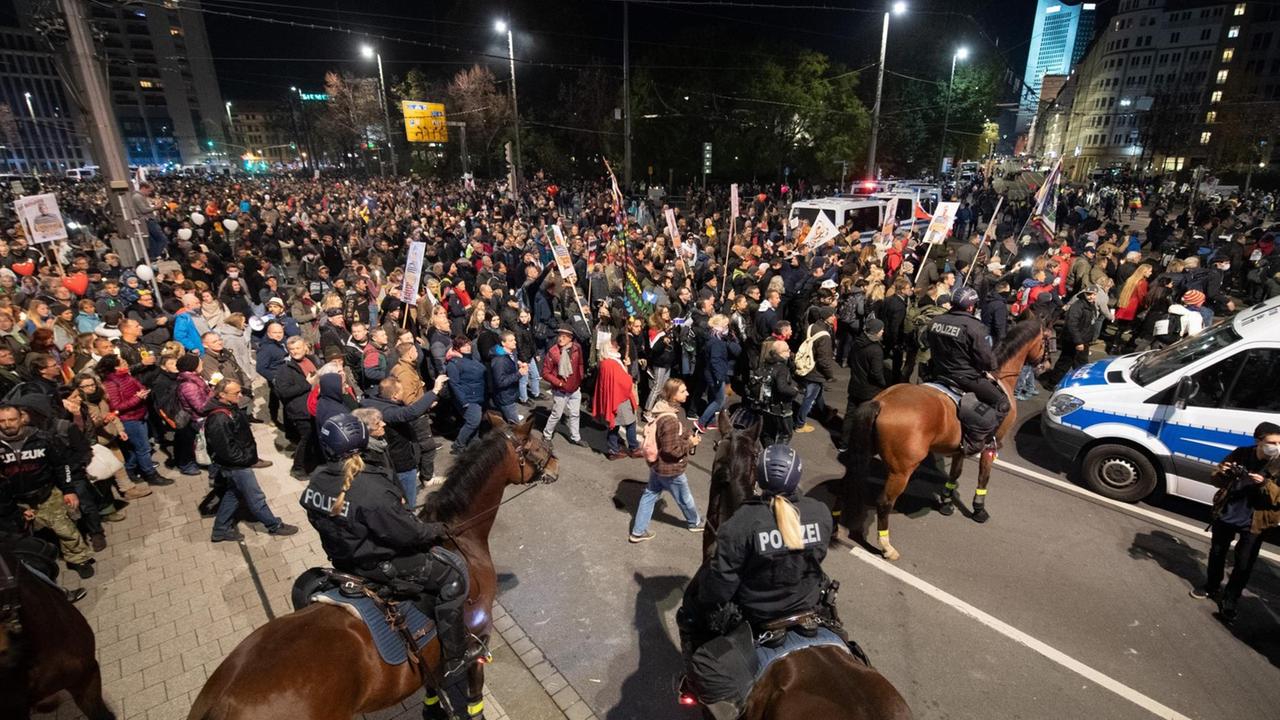 Demonstranten stehen in Leipzig am Haupt-Bahnhof hinter Polizisten auf Pferden.