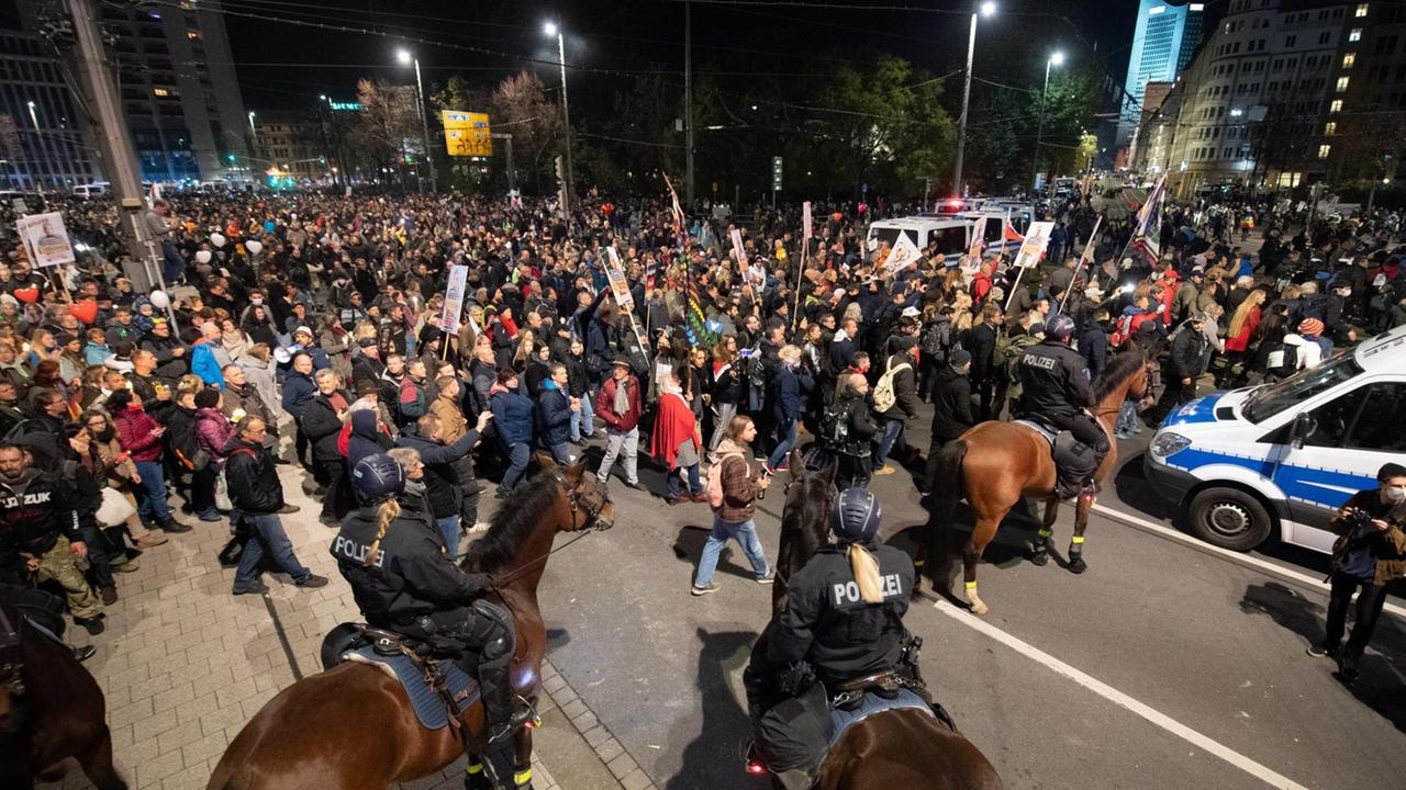 Teilnehmer stehen nach dem Ende einer Demonstration der Stuttgarter Initiative "Querdenken" am Hauptbahnhof hinter der Reiterstaffel der Polizei.