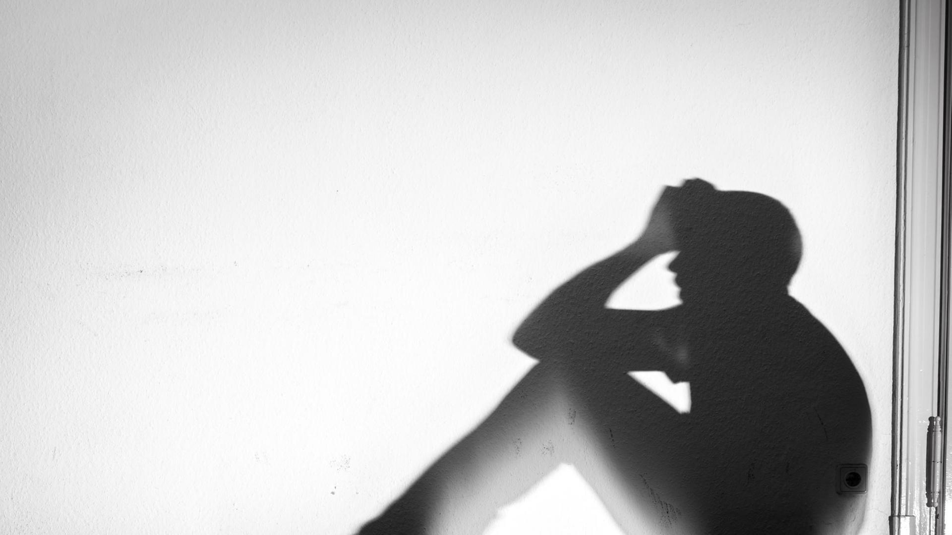 Der Schatten eines Mannes in verzweifelter Haltung wird an eine weiße Wand geworfen, aufgenommen am 01.02.2015 in Dresden (Sachsen)