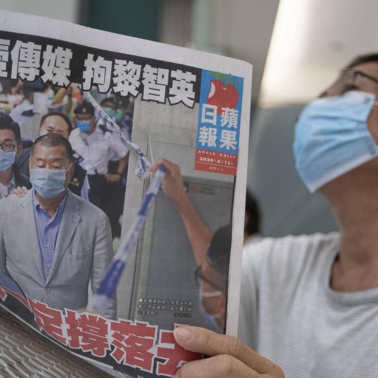 Ein Mann mit einem Mund-Nase-Schutz liest eine Ausgabe der "Apple Daily".