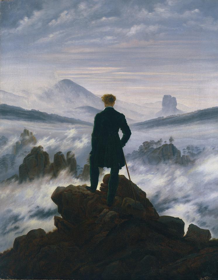Ein Mann steht auf einem Berg und blickt in ein Nebelmeer aus dem Bergspitzen herausragen.