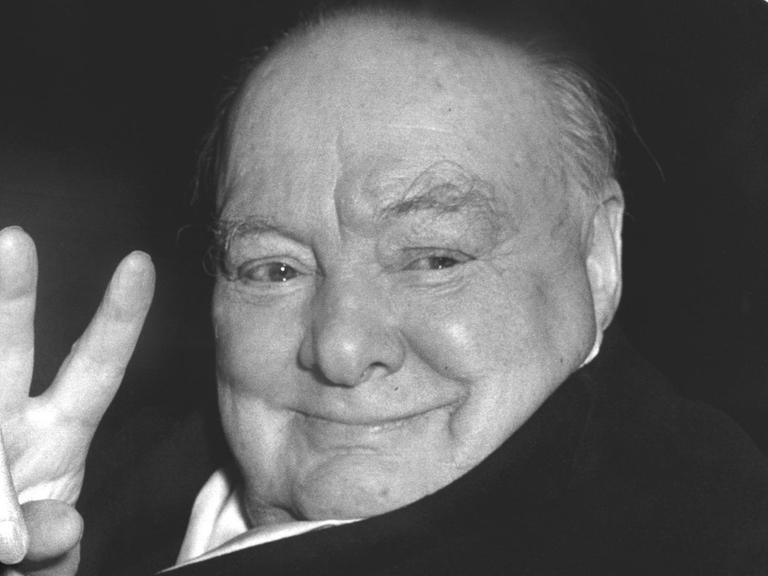 Der britische Staatsmann Sir Winston Churchill (1874-1965) grüßt aus einem Fahrzeug heraus mit der für ihn typischen Geste, dem Victory-Zeichen.