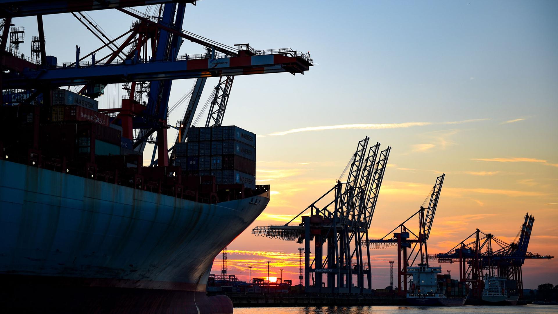 Die Sonne geht in Hamburg im Hafen hinter den Kränen der Containerverladung unter.