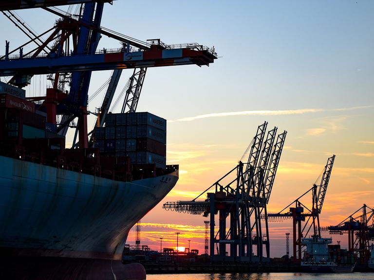Die Sonne geht in Hamburg im Hafen hinter den Kränen der Containerverladung unter.