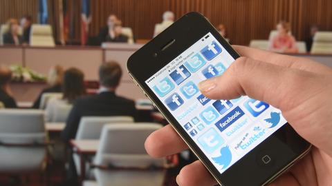 Eine Person hält ein Smartphone in der Hand, auf dem die Logos von Facebook und Twitter zu sehen sind. 