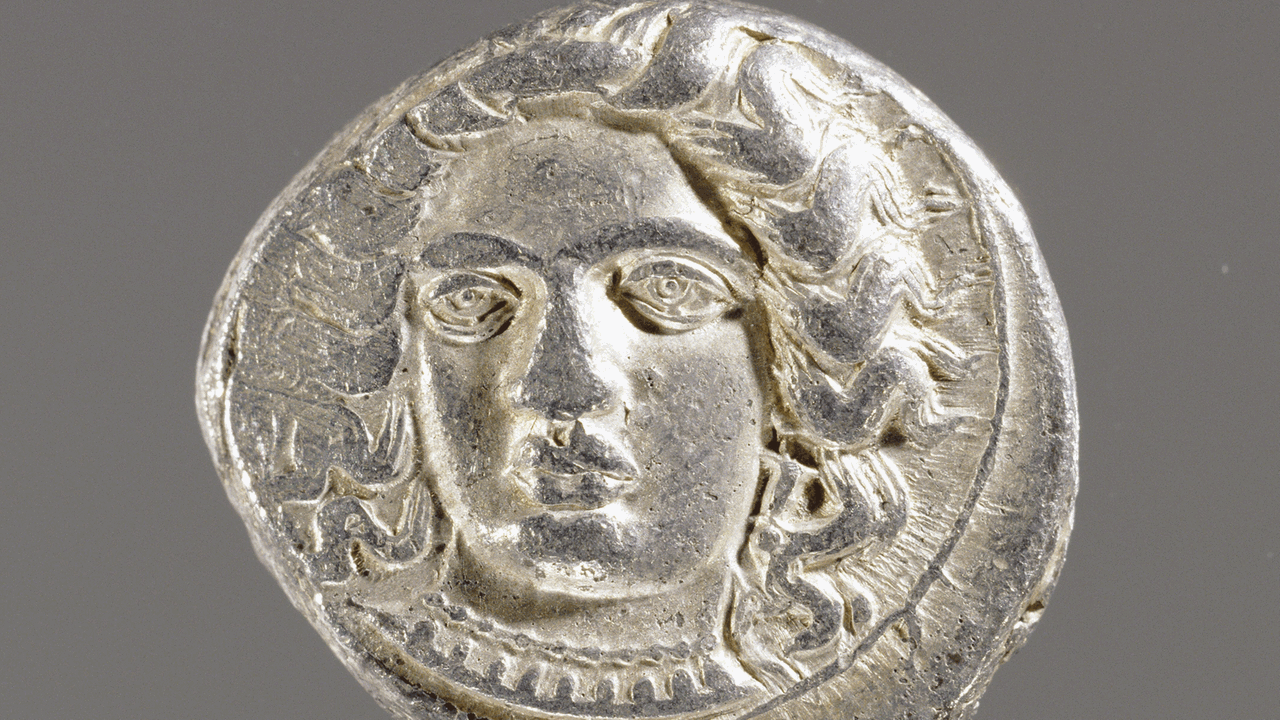 Die Münze zeigt einen Kopf, er von prächtigen Locken umgeben ist.