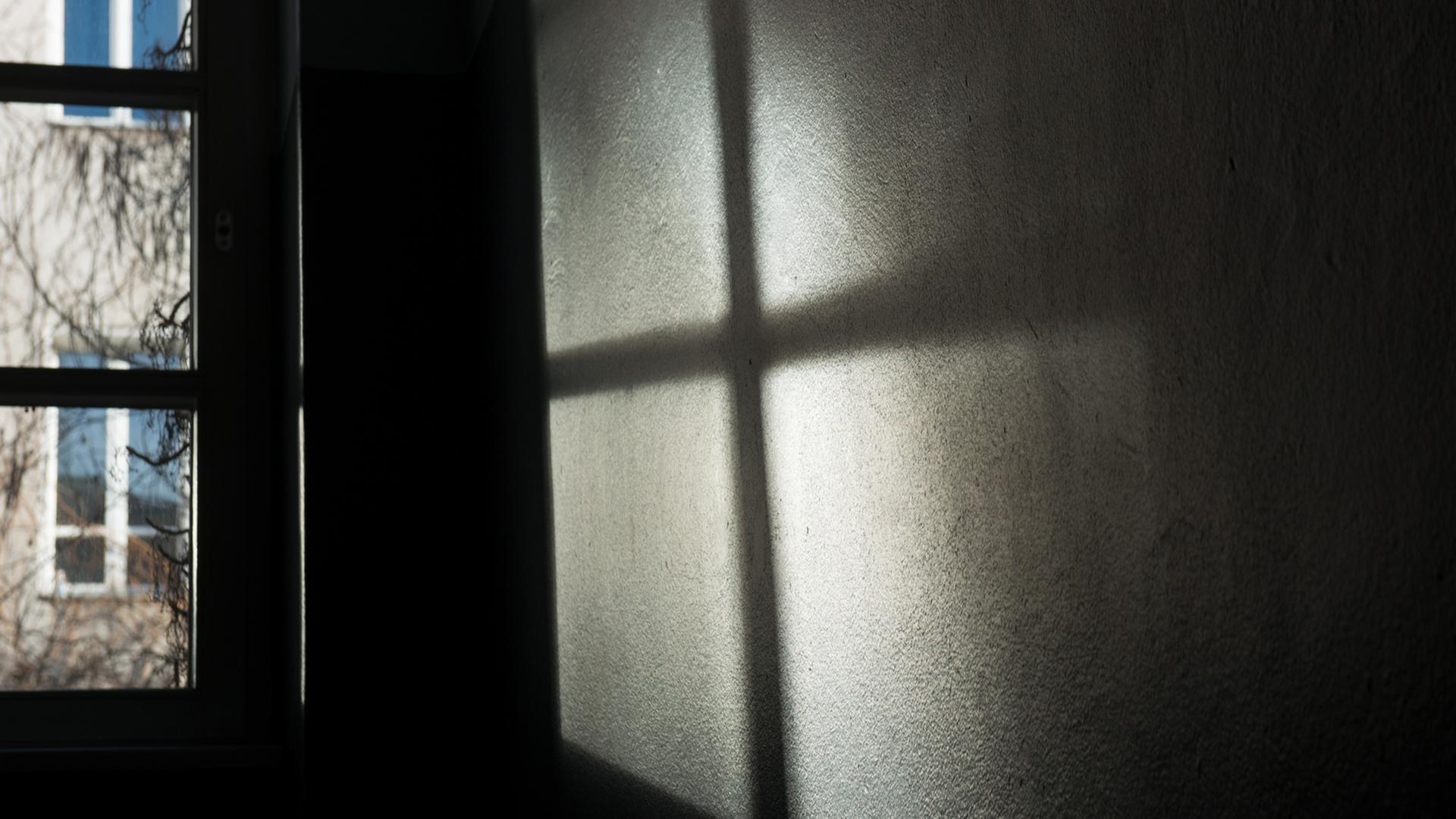 Ein Fenster wirft seinen Schatten auf die Wand. Es entsteht ein dunkles Kreuz.