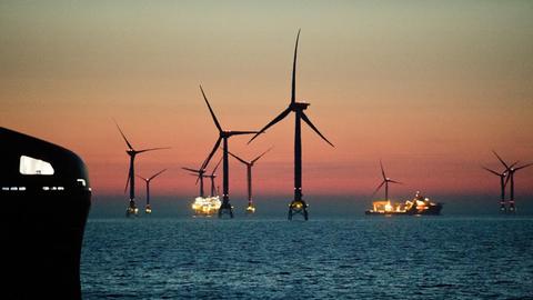 Mehrere Windräder stehen in der Ostsee vor der Insel Rügen. Der Himmel strahlt rötlich.