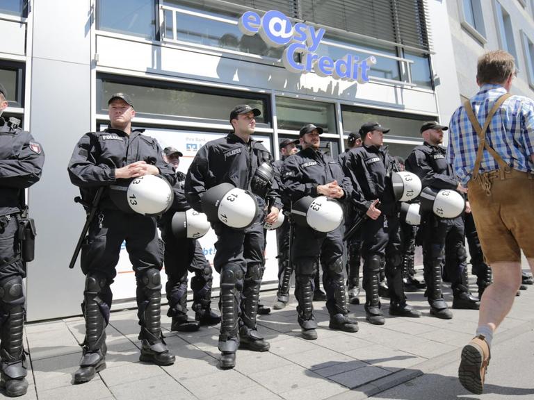 Ein Mann in Lederhose geht am 04.06.2015 in München (Bayern) bei einer Demonstration gegen den G7-Gipfel an Polizisten vorbei, die ein Bankgebäude schützen.