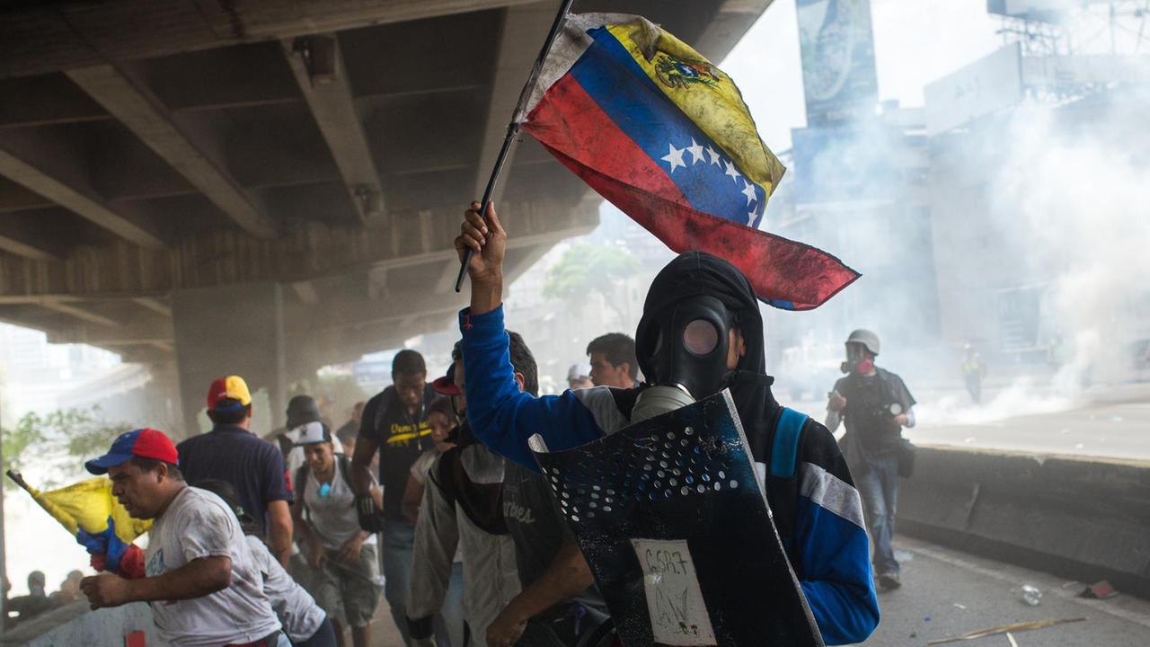 Sie sehen einen Demonstranten mit Maske, der vor Tränen-Gas wegläuft.