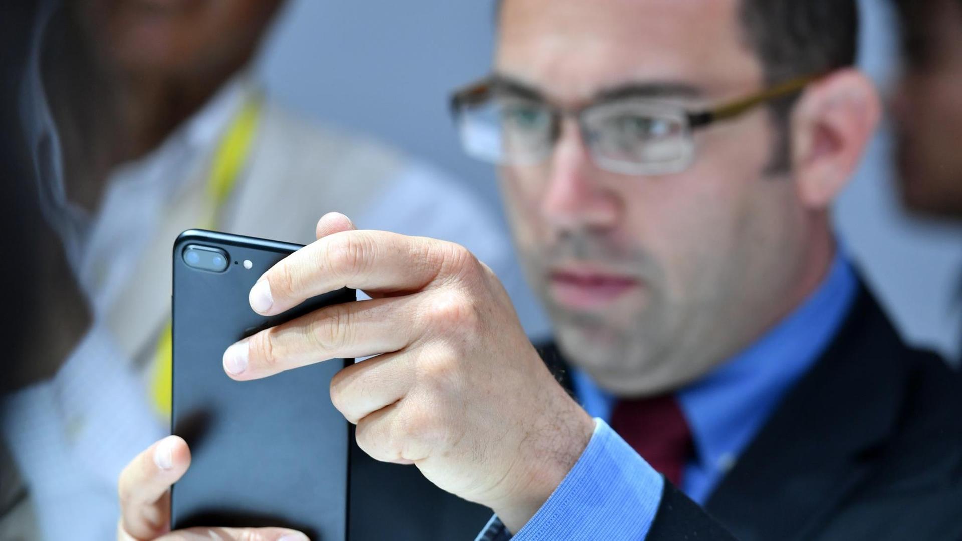 Ein Mann betrachtet ein schwarzes Apple iPhone.