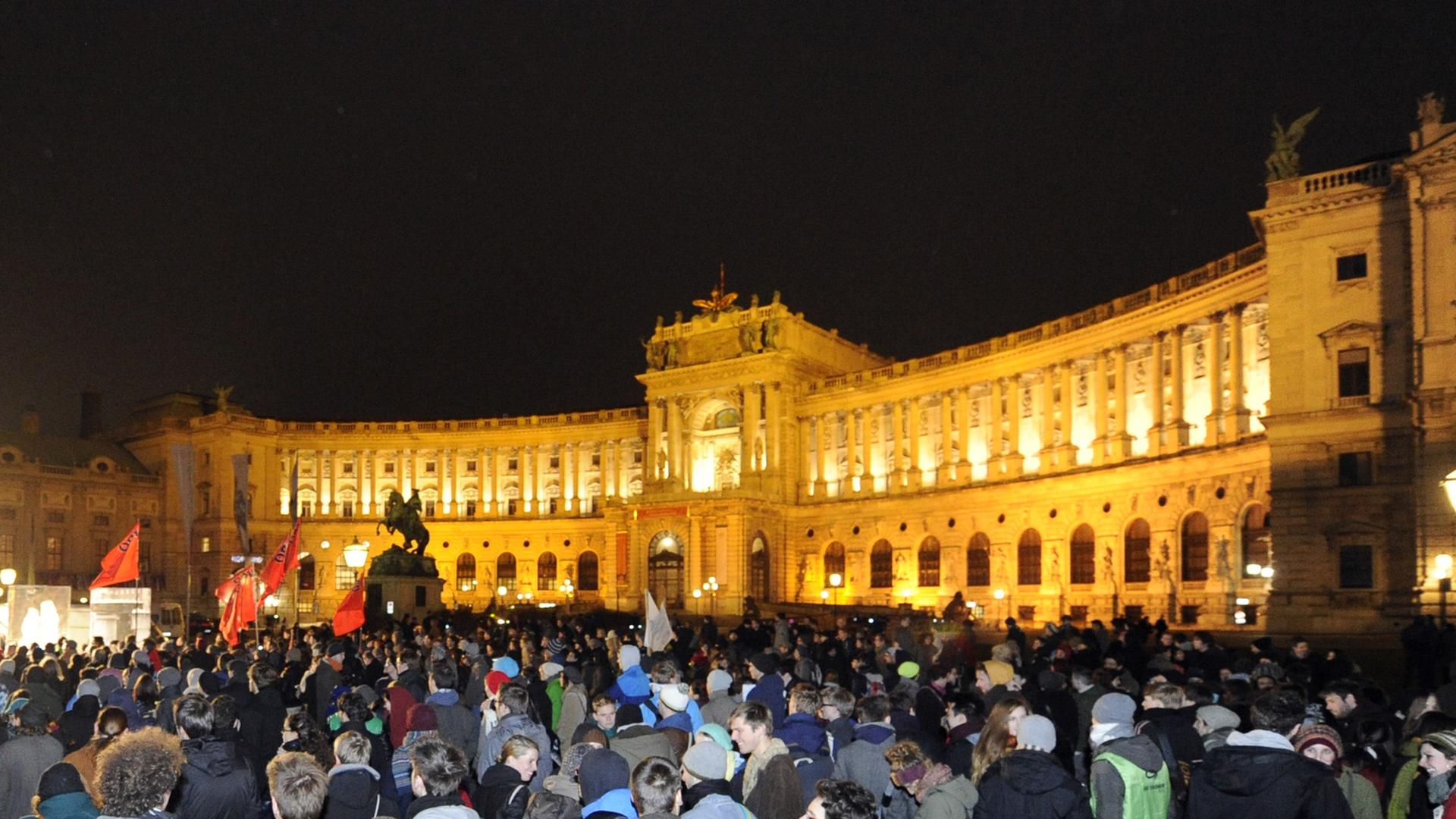 Hunderte Demonstranten bei Nacht vor der erleuchteten Wiener Hofburg.