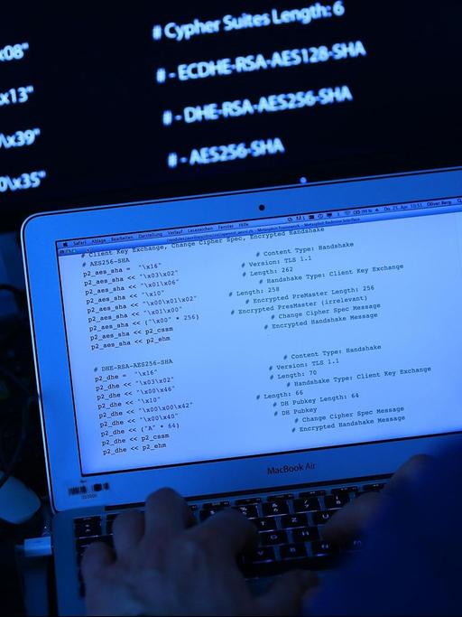 Ein Mann sitzt vor einem Rechner mit Computer Quellcode auf dem Bildschirm.