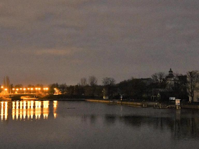 Eine Brücke über die Spree ist nachts beleuchtet, während am Ufer die Häuser und eine Kirche wegen eines Stromausfalls im Dunkeln liegen.