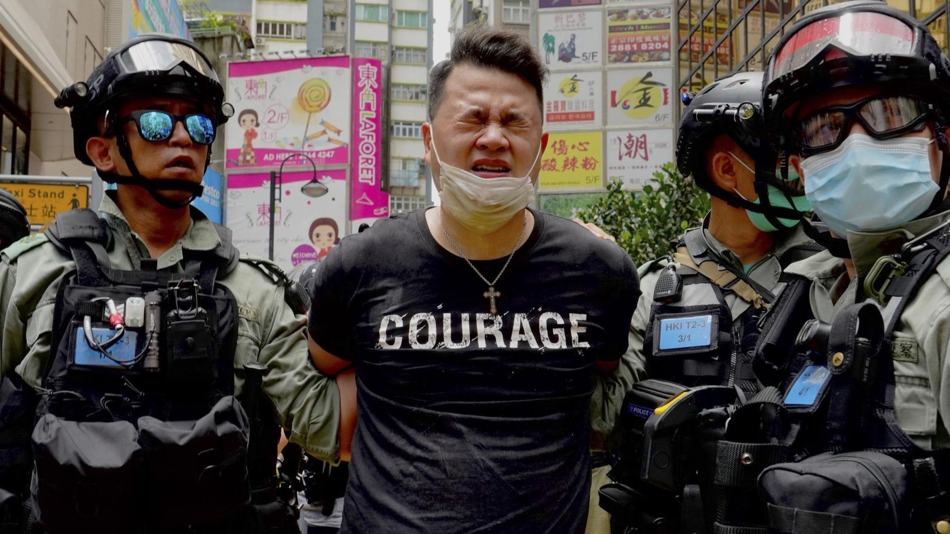 Ein Demonstrant wird in Hongkong von zwei Polizisten abgeführt. Auf dem T-Shirt des Verhafteten ist "Courage" zu lesen.