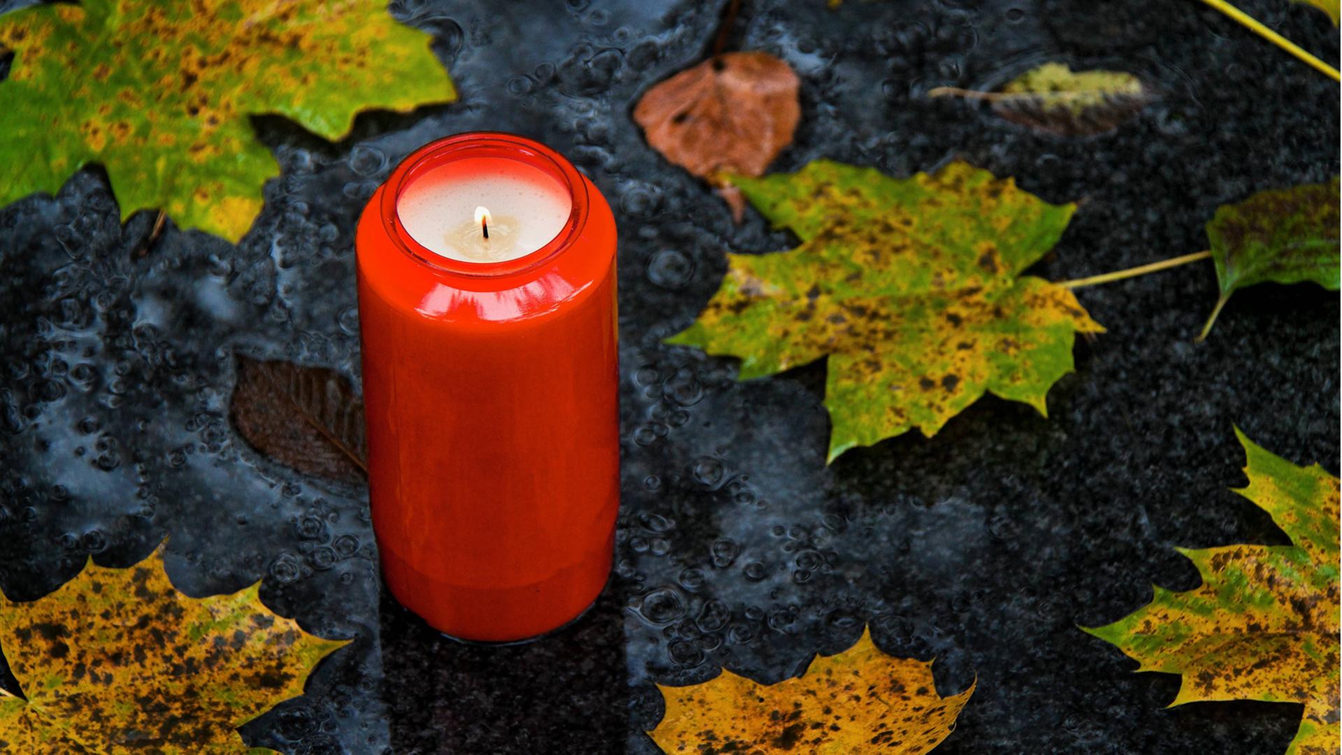 Ein Grablicht zu Allerheiligen im Herbst mit Blättern