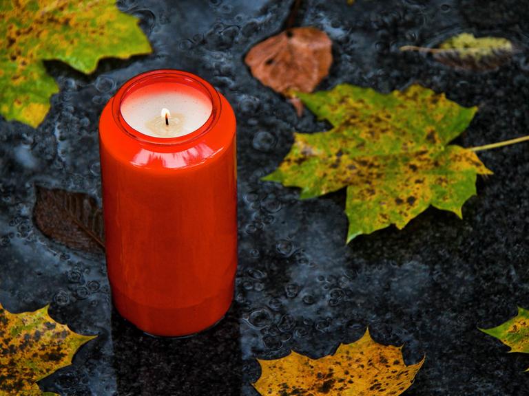 Ein Grablicht zu Allerheiligen im Herbst mit Blättern