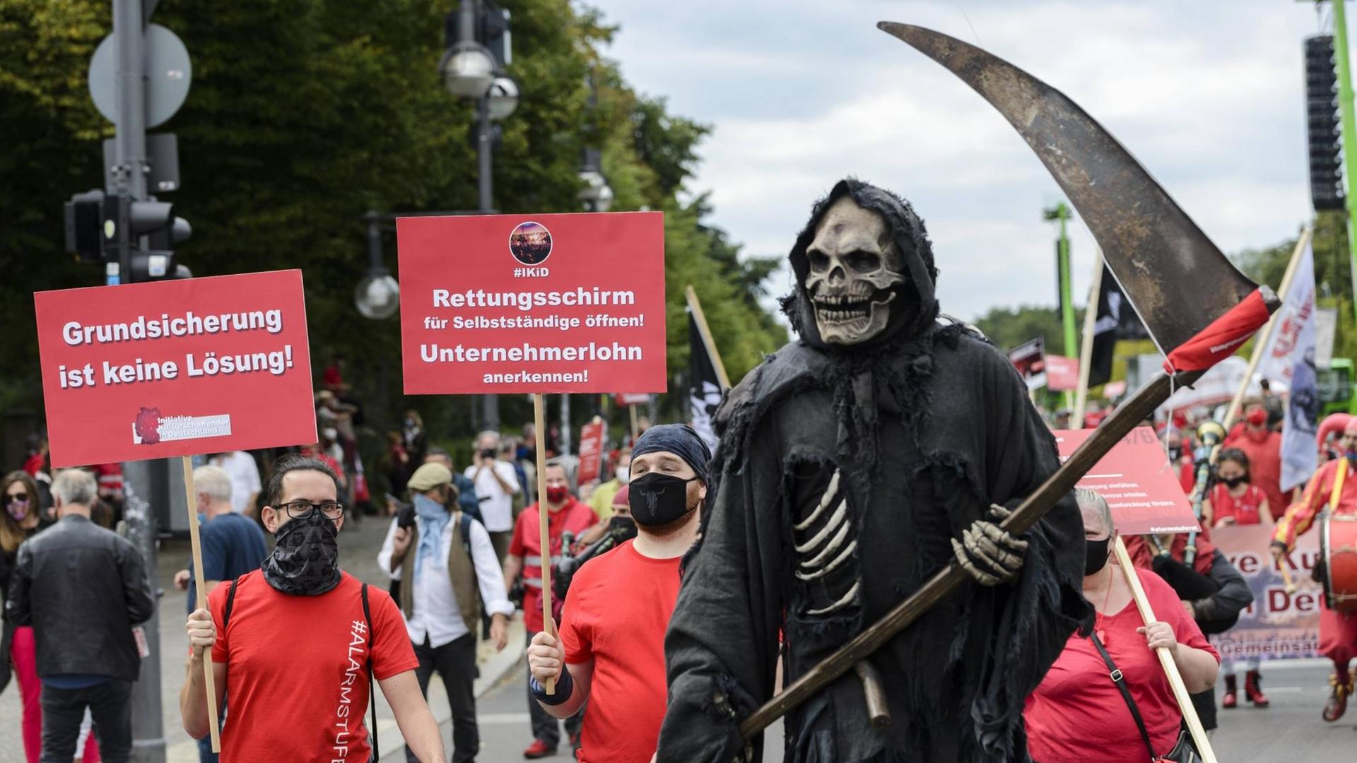 Rot gekleidete Protestierende der Veranstaltungsbranche ziehen durch Berlin, im Vordergrund ein als Sensenmann verkleideter Demonstrant