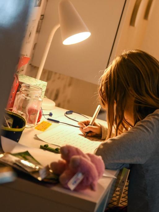 Ein Mädchen sitzt zu Hause an ihrem Schreibtisch und macht Aufgaben für die Schule.