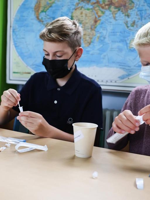 Kinder mit Gesichtsmasken in einem Klassenzimmer führen einen Coronatest durch.