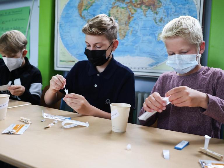 Kinder mit Gesichtsmasken in einem Klassenzimmer führen einen Coronatest durch.