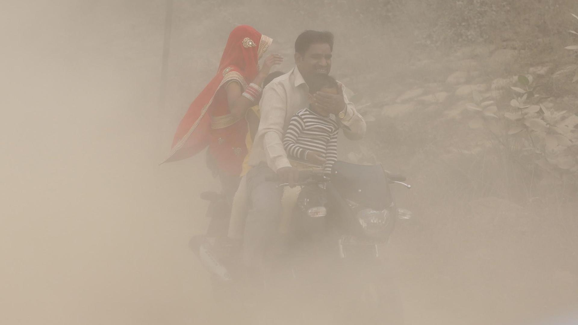 Eine indische Familie auf einem Motorrad mitten in dichtem Smog.