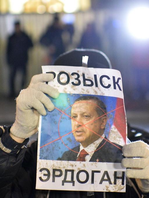 Ein Demonstrant hält ein Plakat des türkischen Präsidenten Erdogan in die Kamera. Über Erdogans Gesicht liegt ein rotes Kreuz wie von einem Zielradar.