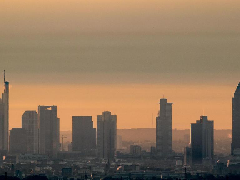 Die Hochhäuser von Frankfurt am Main (Hessen) sind im Licht der aufgehenden Sonnen im morgendlichen Dunst beim Blick von Kronberg im Taunus zu sehen.