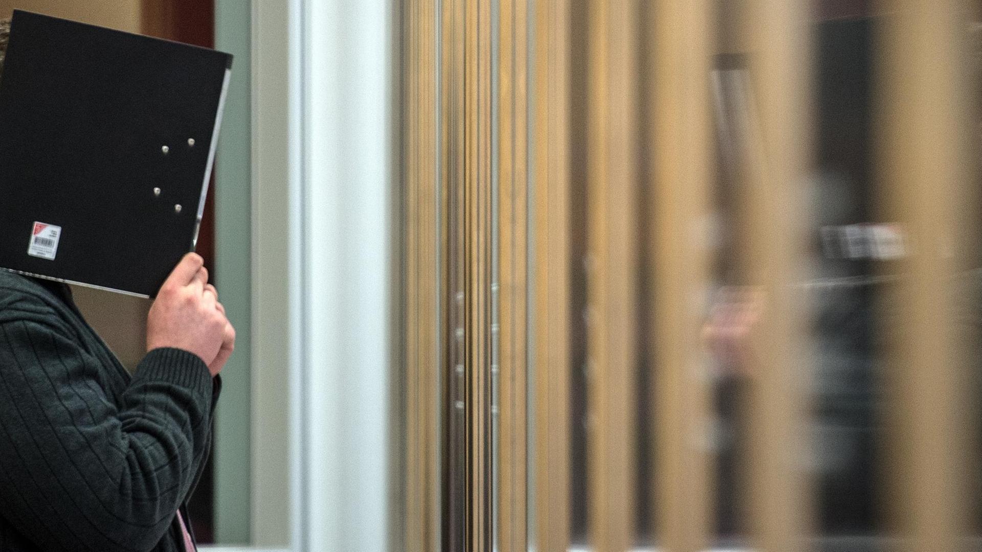 Der Angeklagte Nils D. hält sich in Düsseldorf im Gerichtsaal einen Aktenordner vor das Gesicht