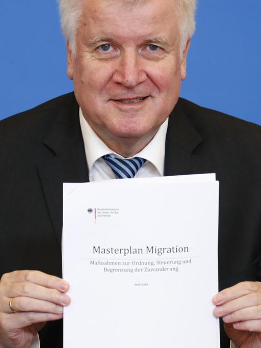 Seehofer hält ein Exemplar des "Masterplan Migration" in die Kamera.