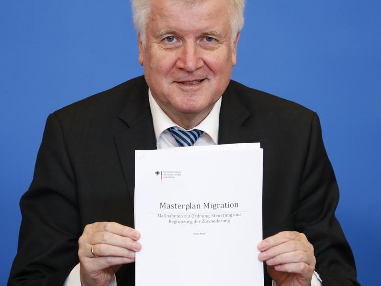 Seehofer hält ein Exemplar des "Masterplan Migration" in die Kamera.