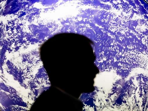 Ein Mann sitzt bei der UN-Klimakonferenz COP26 vor einem leuchtenden Globus.