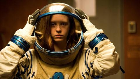 Frau im Astronautenanzug setzt sich ihren Helm auf