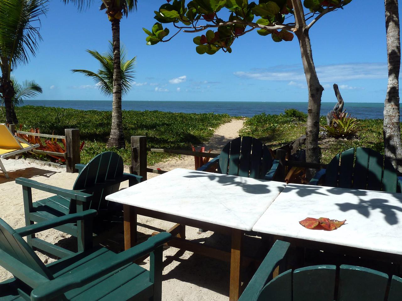Tische und Stühle stehen auf eine Veranda unter Bäumen und mit Blick auf den Strand und das Meer.