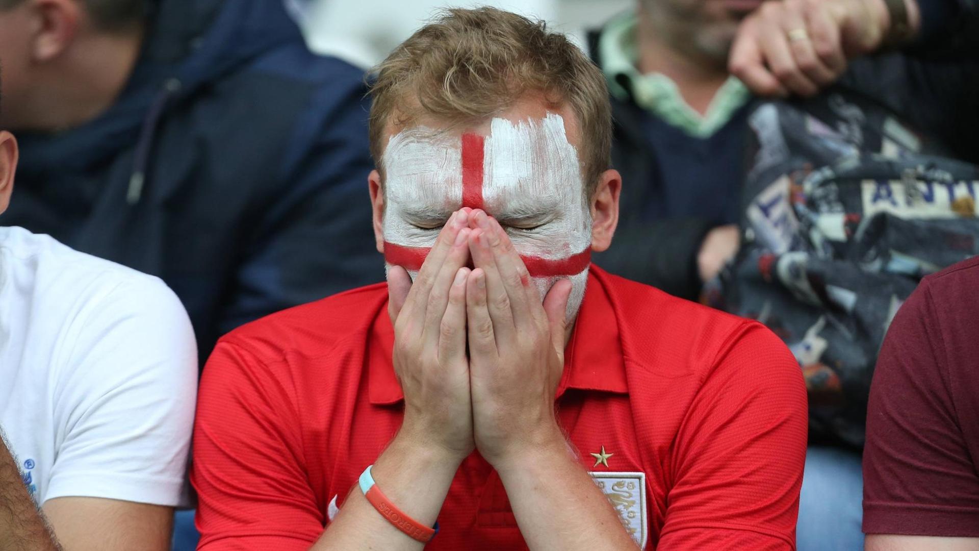 Ein England-Fan mit englischer Flagge als Gesichtsbemalung hält die Hände ins Gesicht.