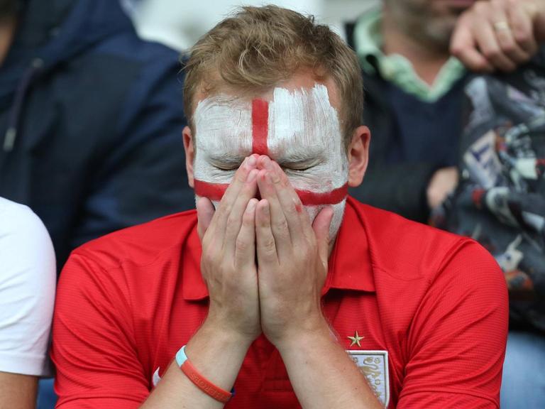 Ein England-Fan mit englischer Flagge als Gesichtsbemalung hält die Hände ins Gesicht.