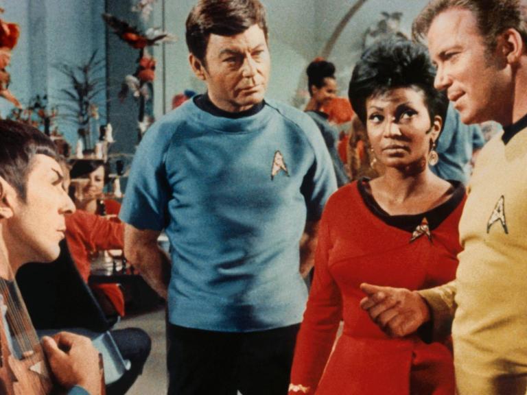 Szene aus der US-Fernsehserie "Star Trek" (1966-1969): Die Schwarze Schauspielerin Nichelle Nichols sowie die Schauspieler Leonard Nimoy, Deforest Kelley und William Shatner sprechen miteinander.