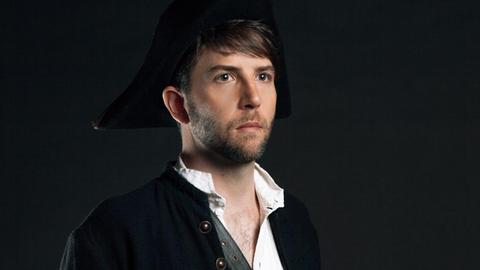 Owen Pallett steht mit weißem Hemd und schwarzer Jacke vor einem schwarzen Hintergrund