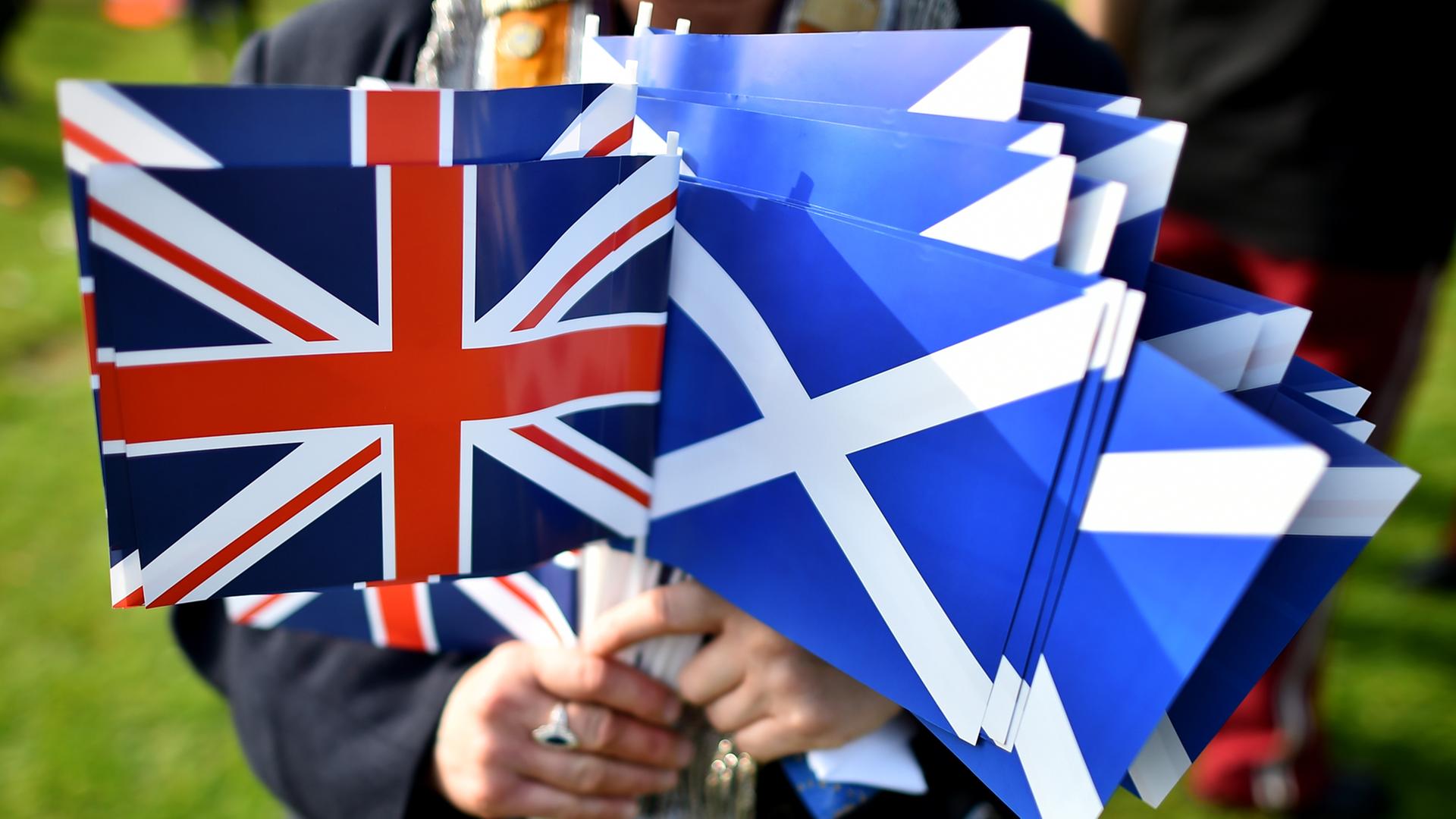 Eine Person hält mehrere Papierflaggen in der Hand. Sowohl welche mit Schottlands Wappen als auch dem Union Jack.